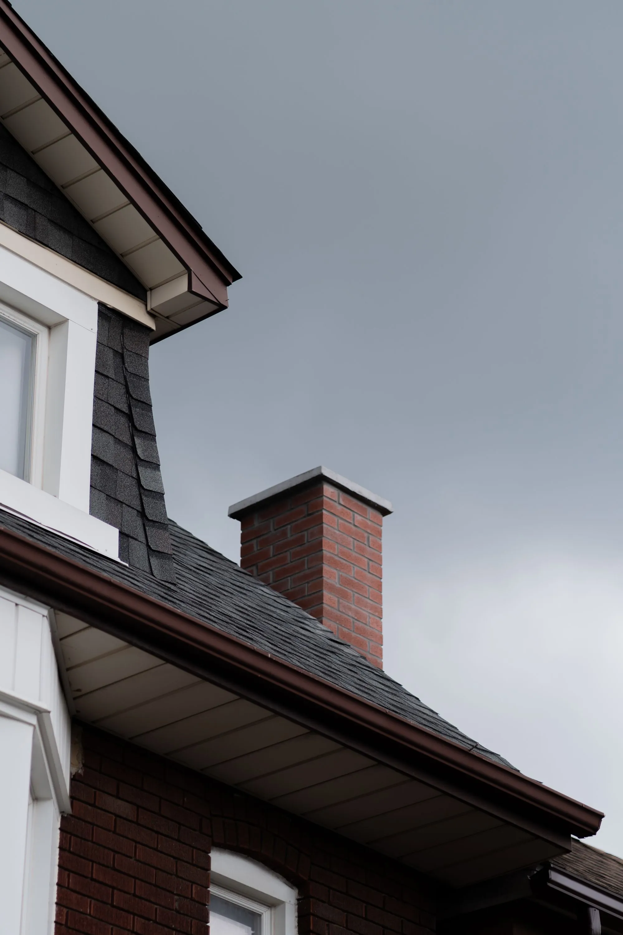 A dormer and a brick chimney rising from a shingled roof