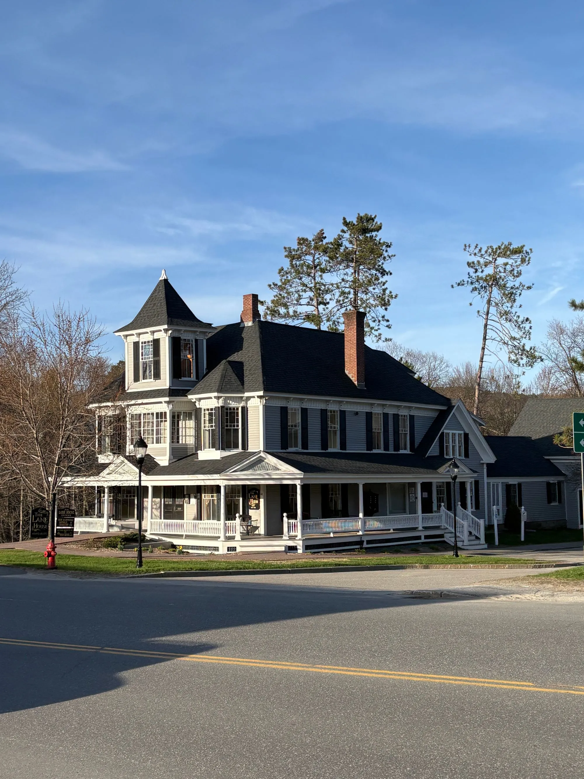 A white clapboard house with a wrap-around porch and a dark roof
