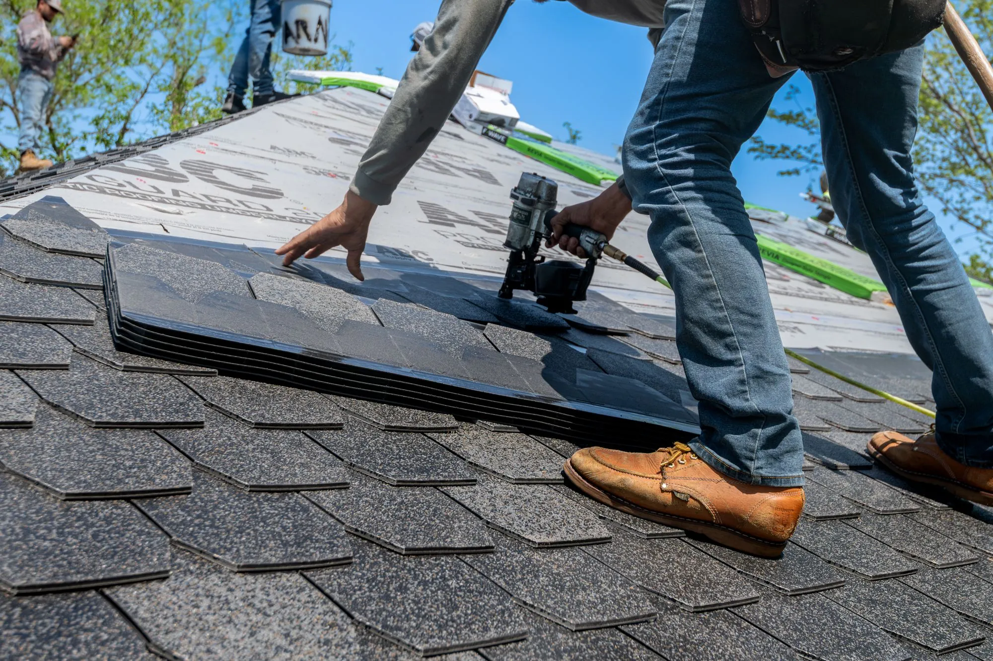 A roofer running a nail gun along a course of shingles
