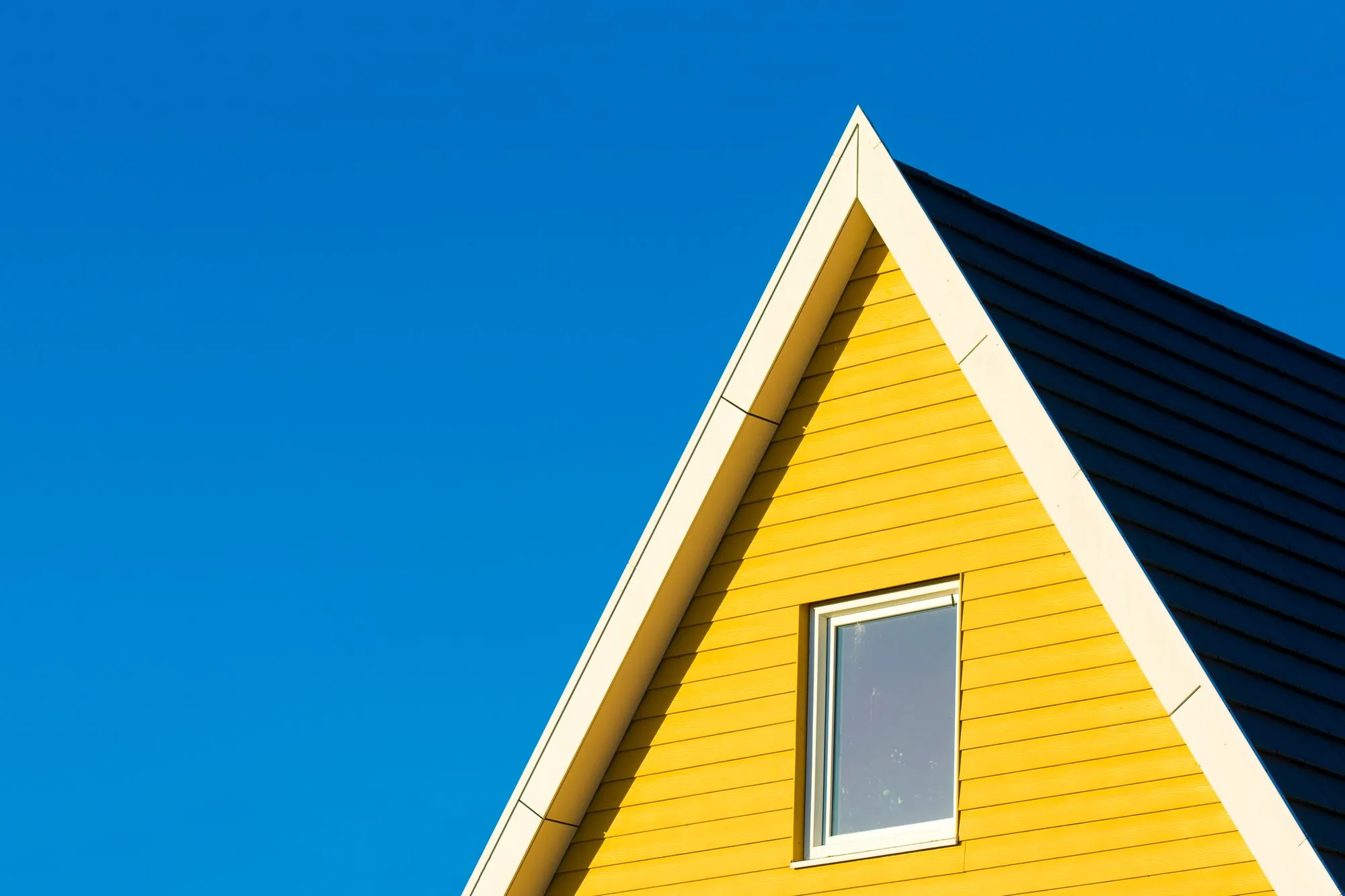 The gable end of a yellow house meeting a clear blue sky