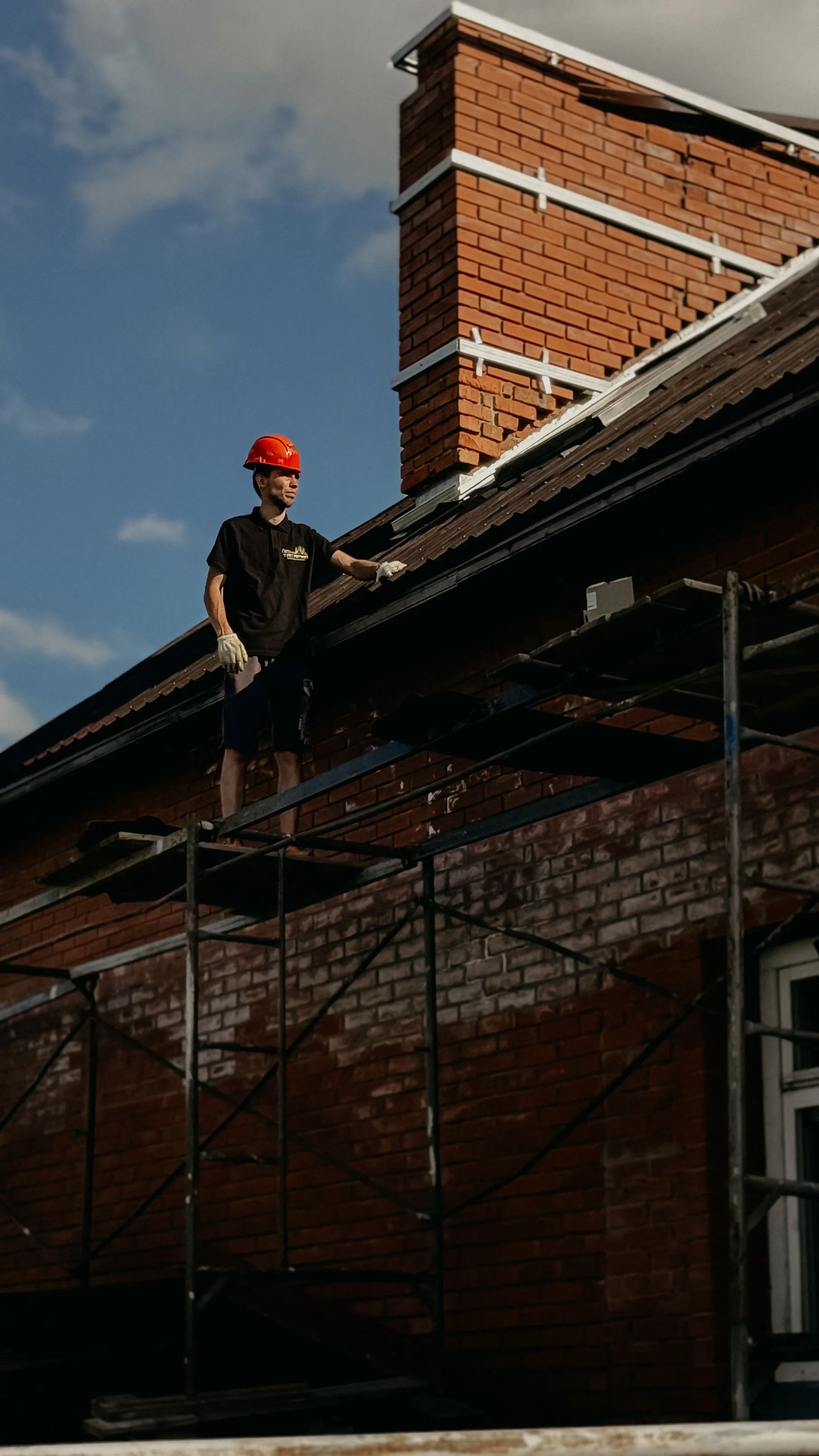 A roofer working along the eaves of a brick house from scaffolding