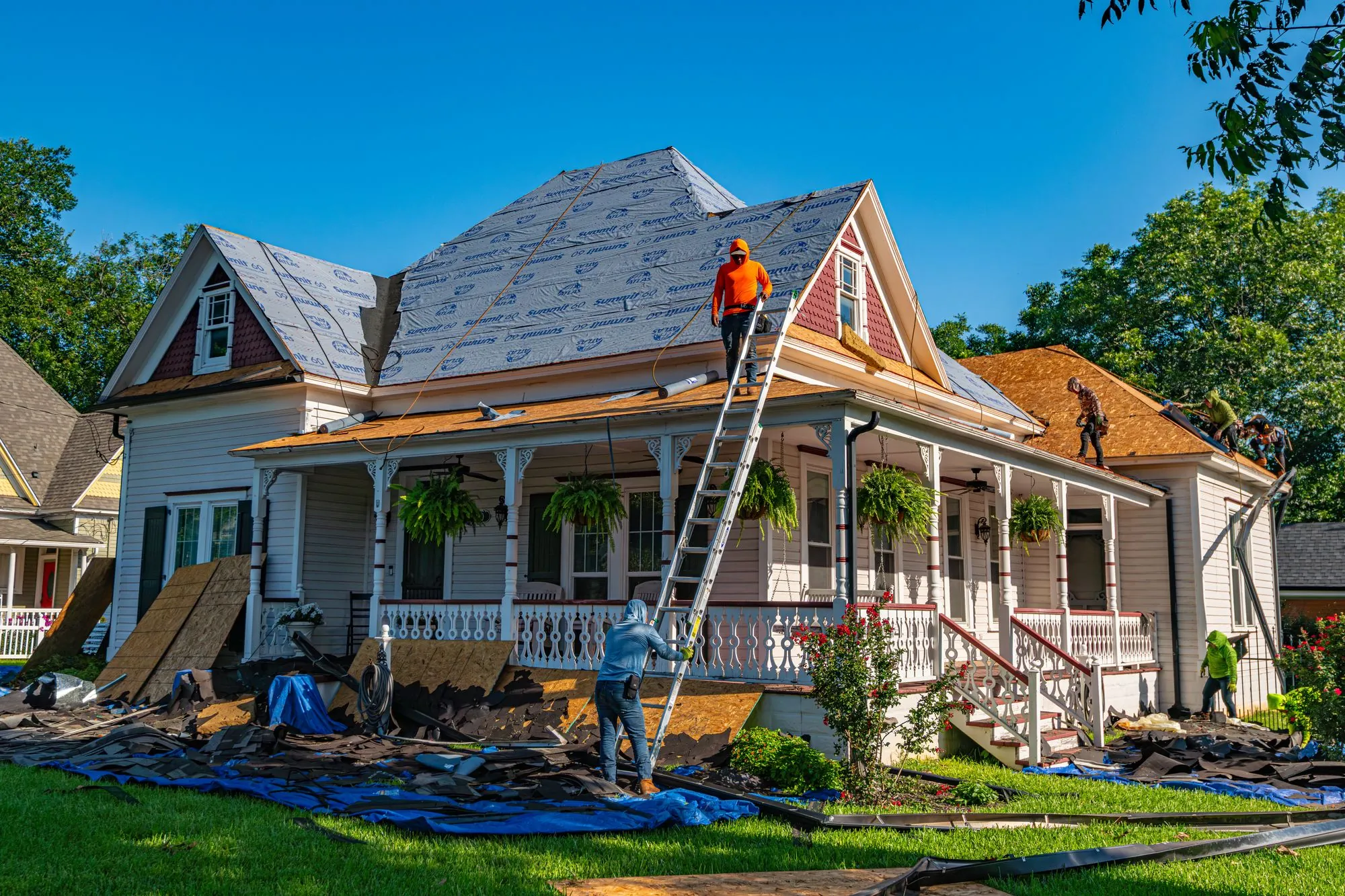 A white house with a crew and ladders at work on the roof